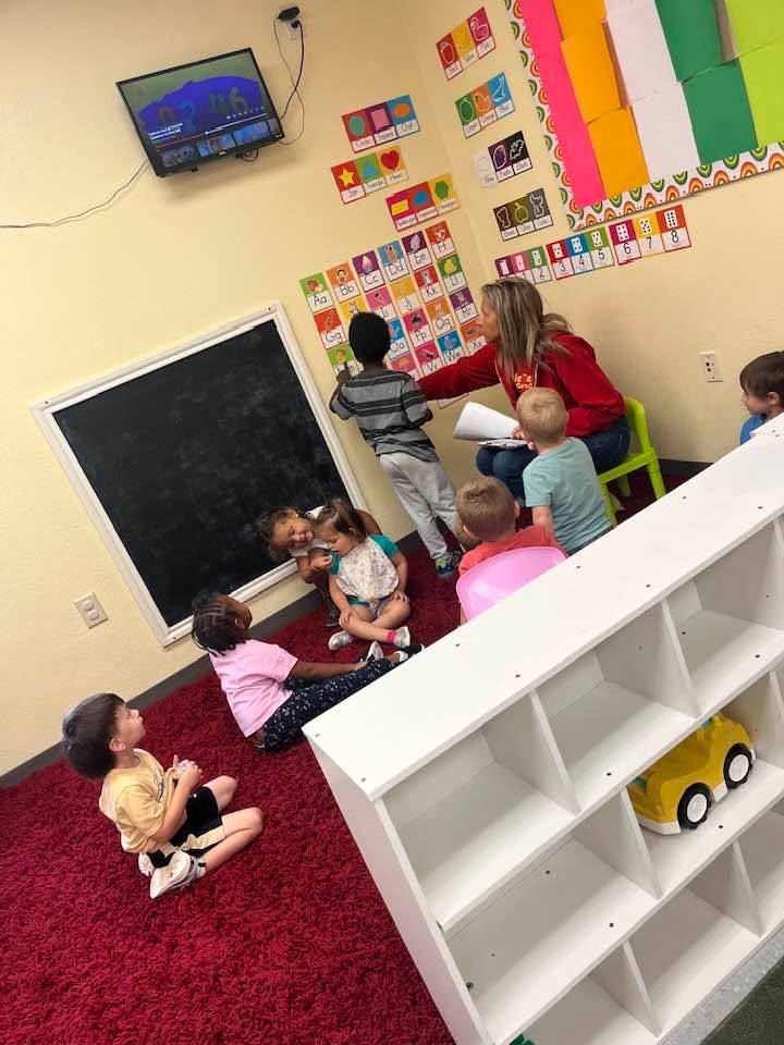 A teacher reading with a small group of children on a red rug in a colorful classroom