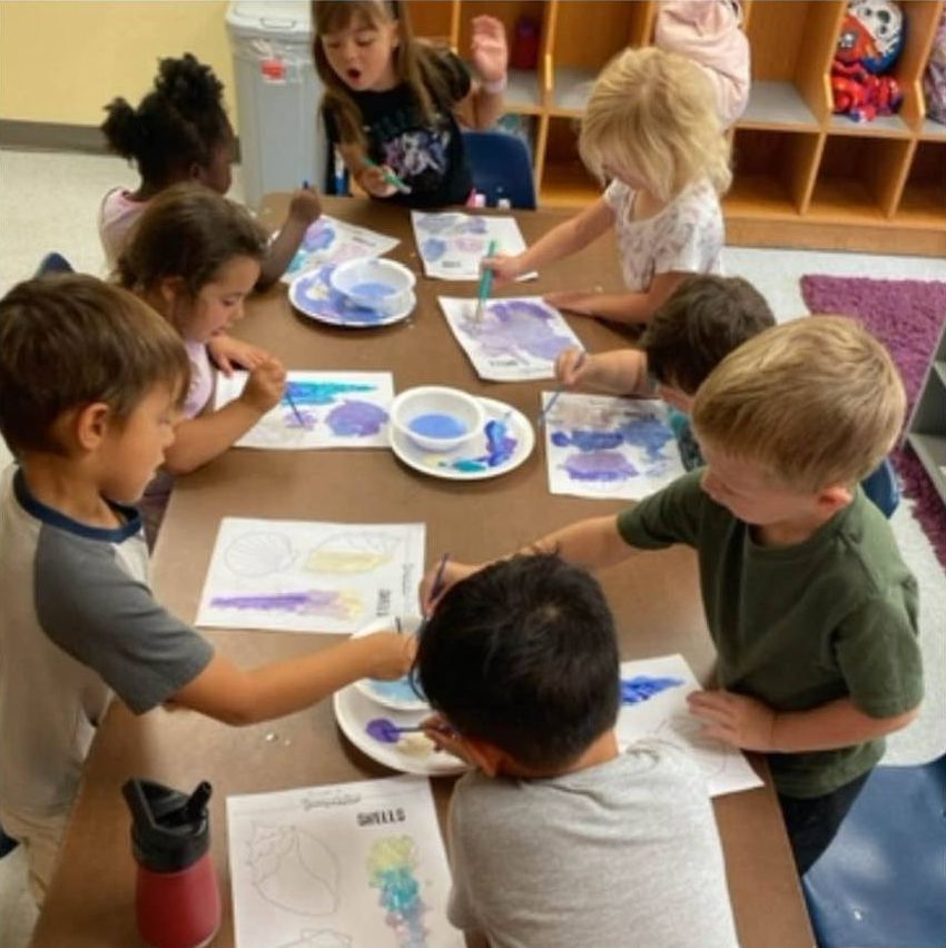 Children painting paper plates together at a classroom table