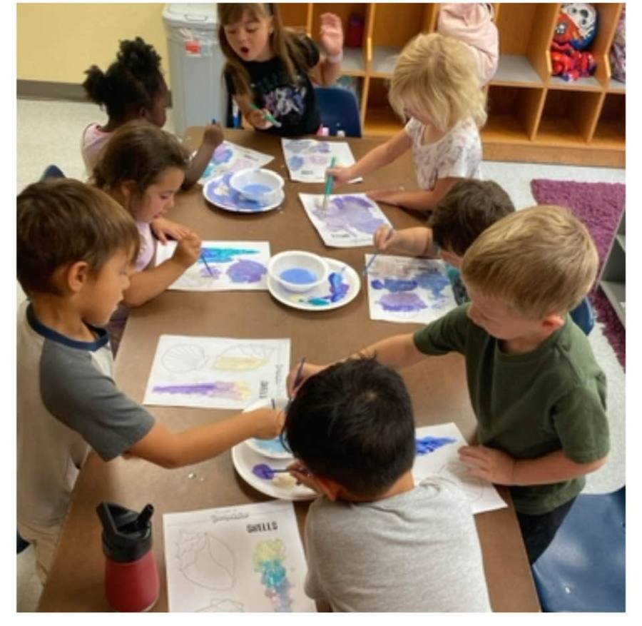 Children painting paper plates together at a classroom table